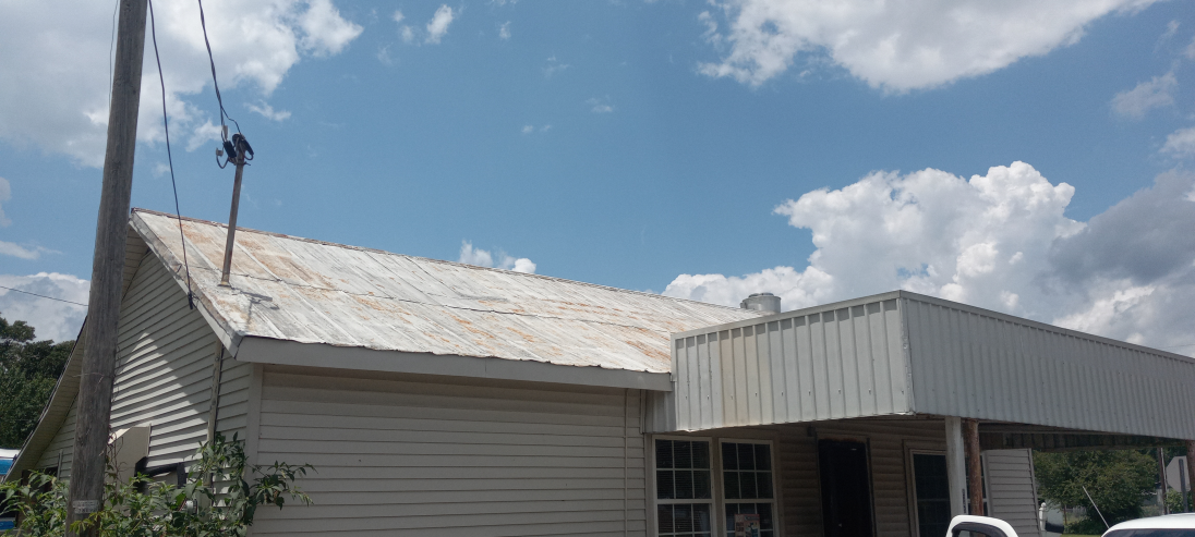 A Damaged, Old Metal Roof Sustaining More Damage Under a Clear, Sunny Sky